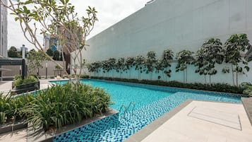 A swimming pool with a tiled edge, surrounded by greenery and a modern building facade.
