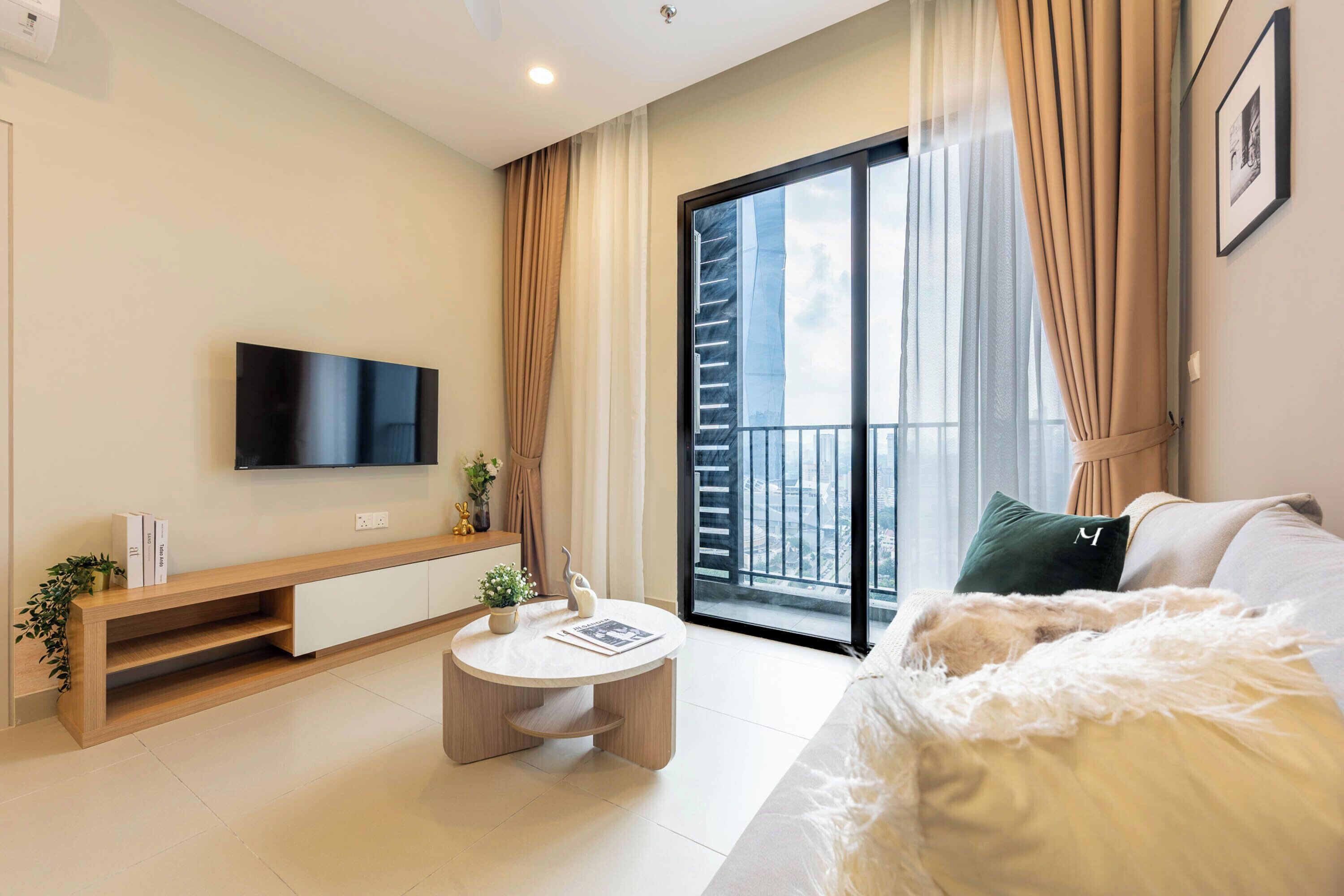 A modern living room with a flat-screen TV, a round coffee table, a sofa, and a balcony with a view of the city.