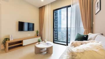 A modern living room with a flat-screen TV, a round coffee table, a sofa, and a balcony with a view of the city.