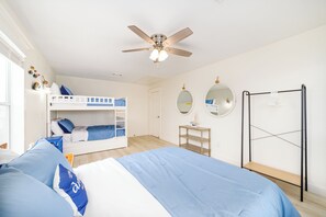 Un dormitorio con literas, ventilador de techo, armario y una mesita.