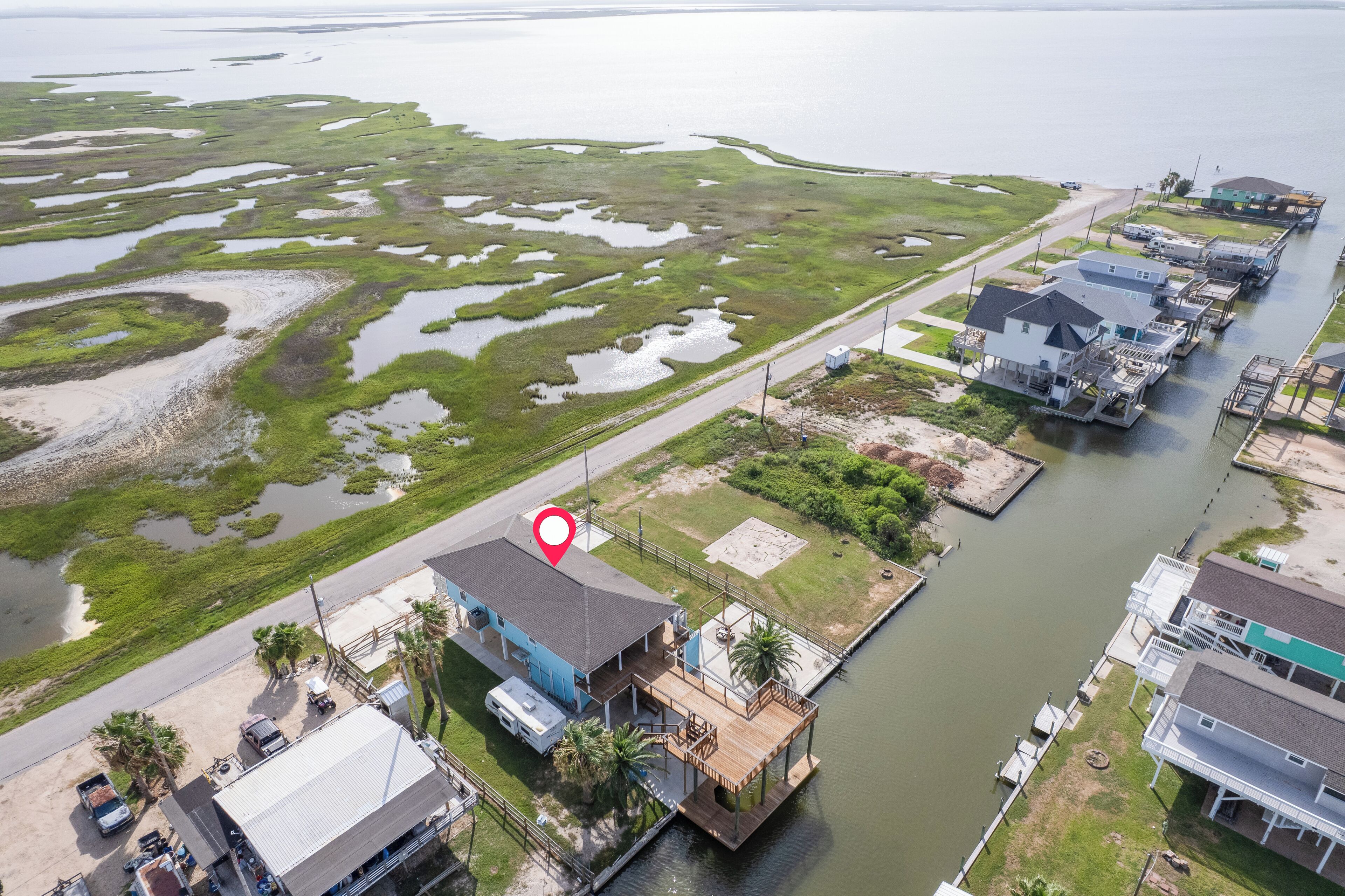 A waterfront property with a dock, a house with a blue roof, and a large body of water with marshy areas.