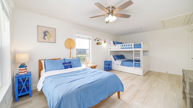 Une chambre avec un lit simple, un lit superposé, un ventilateur de plafond, une fenêtre avec des stores et une lampe fixée au mur.