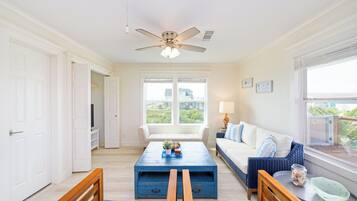 A bright living room with a ceiling fan, a sofa, a coffee table, and a view of the outdoors through large windows.