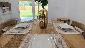 A dining table set for four with white plates, silverware, and a vase with white flowers.