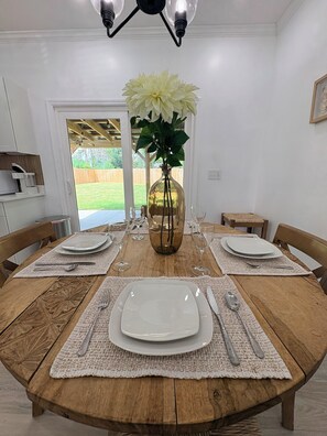Une table à manger dressée pour quatre personnes, avec de l’argenterie, des assiettes blanches et un vase contenant des fleurs blanches.