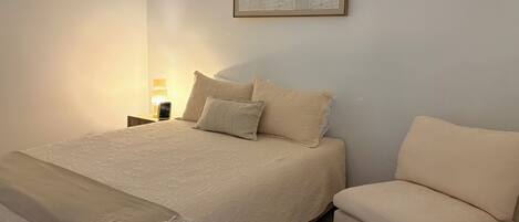 Une chambre à coucher avec un lit, une table de chevet, une lampe et une œuvre d’art encadrée accrochée au mur.