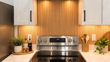 A modern kitchen with stainless steel appliances, wooden paneling, and a digital clock.
