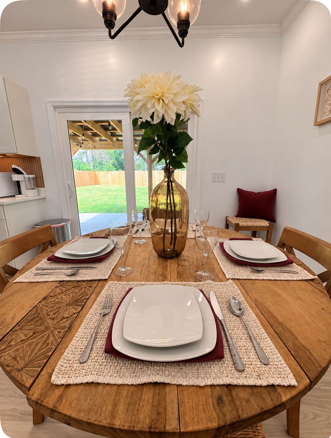 Une table à manger dressée pour quatre personnes, avec des sets de table, des assiettes, des couverts et un vase rempli de fleurs.