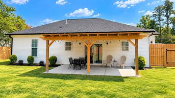 A single-story house with a covered patio area, a lawn, and a wooden fence in the background.