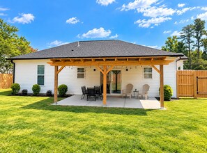 Une maison de plain-pied avec un patio couvert, une pelouse et une clôture en bois en arrière-plan.