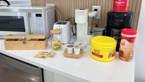 A kitchen counter with a microwave, toaster, coffee maker, and various food items.