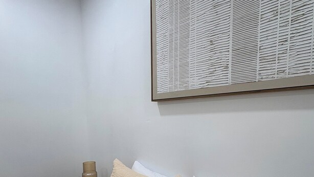 A bedroom with a bed, pillows, a nightstand, a lamp, and a framed artwork on the wall.