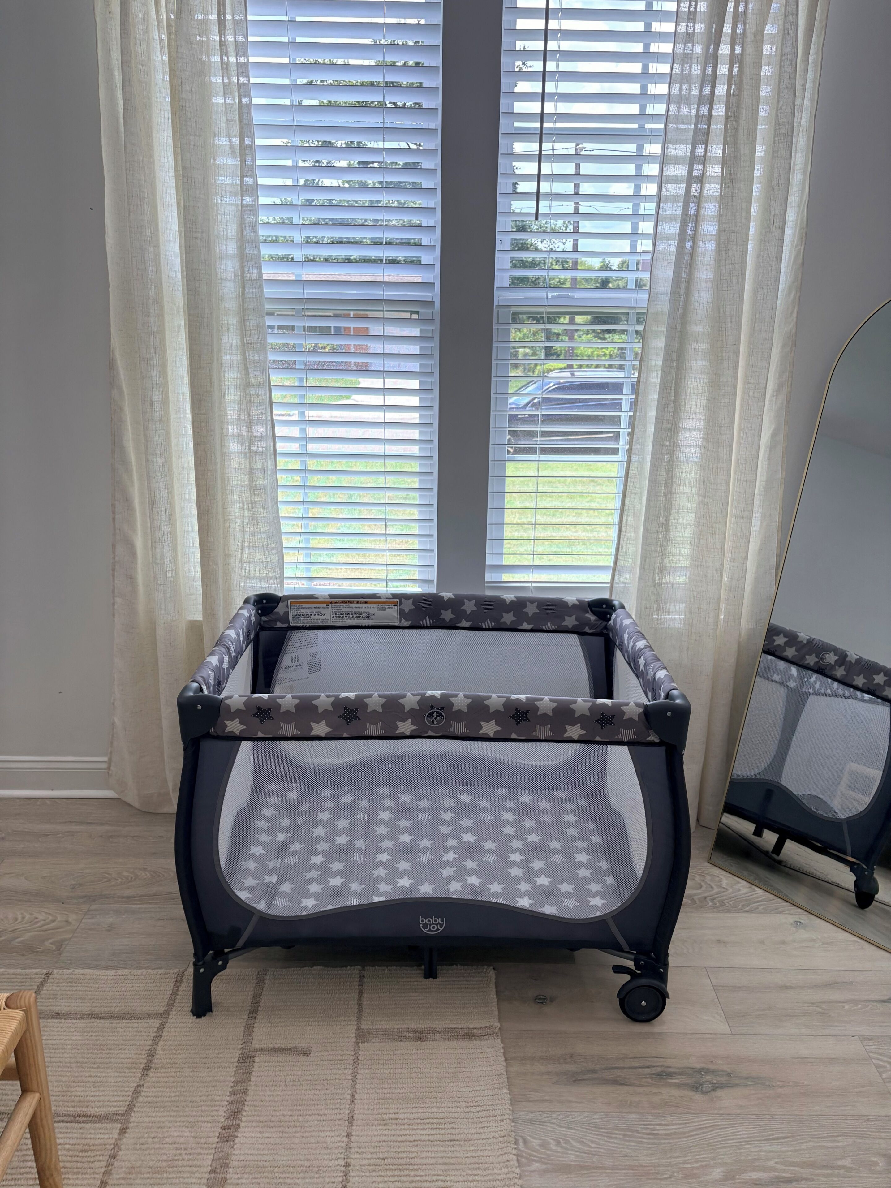 A baby playpen with a star pattern, positioned in a room with a large window and a view of the outdoors.