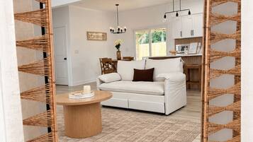 A modern living room with a white sofa, a round wooden coffee table, and a woven rattan partition.