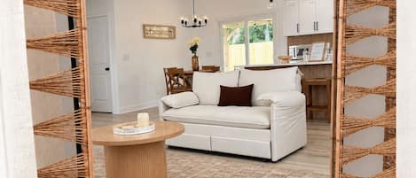 A modern living room with a white sofa, a round wooden coffee table, and a woven rattan partition.