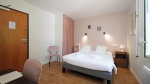 A hotel room with a bed, a desk with a chair, a bedside table, and a door. - Hostellerie Du Clos Pite (Prechacq-les-Bains)