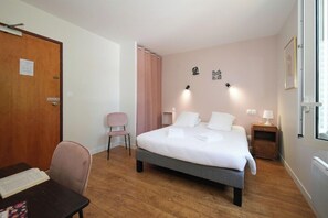 Ett hotellrum med en säng, ett skrivbord med en stol, ett nattduksbord och en dörr.