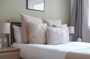 A neatly made bed with multiple pillows and a bedside table with a lamp. - Stylish London Bridge Apartment (London)