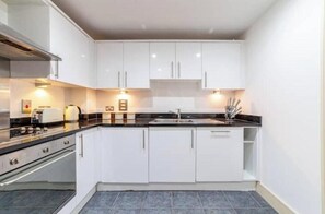A modern kitchen with white cabinets, a black countertop, and a stainless steel range hood. - Stylish London Bridge Apartment (London)