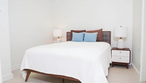 A neatly made bed with a white bedspread, two bedside tables with lamps, and a headboard with pillows. - 2 bedrooms, 2 baths, luxury, most beautiful beach, Ocean view. 46 nights minimum (Nassau)