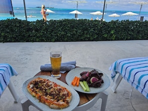 A dining table with a pizza, a glass of beer, and a plate of meat and vegetables. - 2 bedrooms, 2 baths, luxury, most beautiful beach, Ocean view. 46 nights minimum (Nassau)