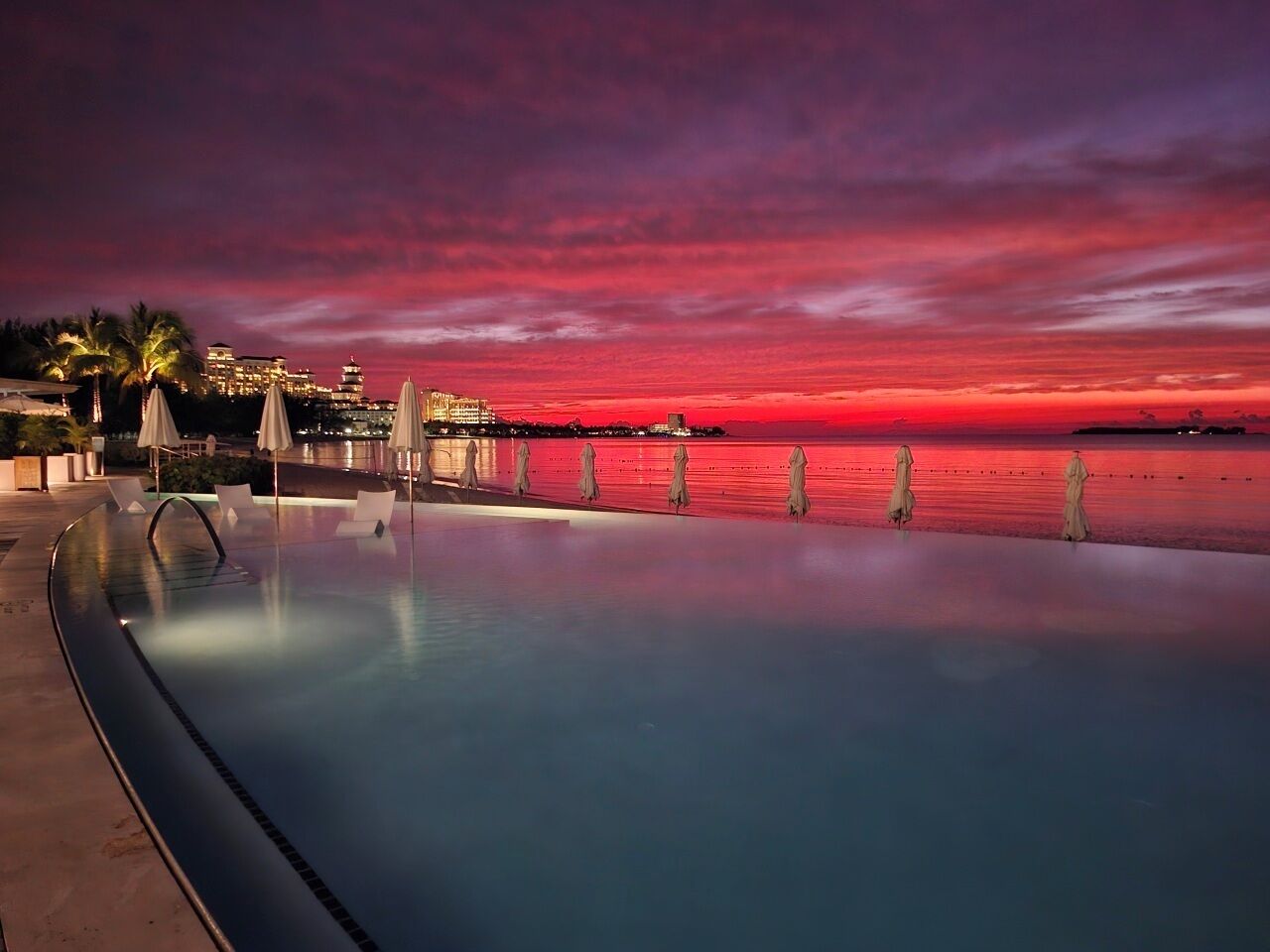A swimming pool with a view of the ocean at sunset.