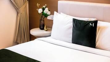 Une chambre d’hôtel avec un lit, une table de chevet, un vase avec des fleurs et une prise électrique au mur.