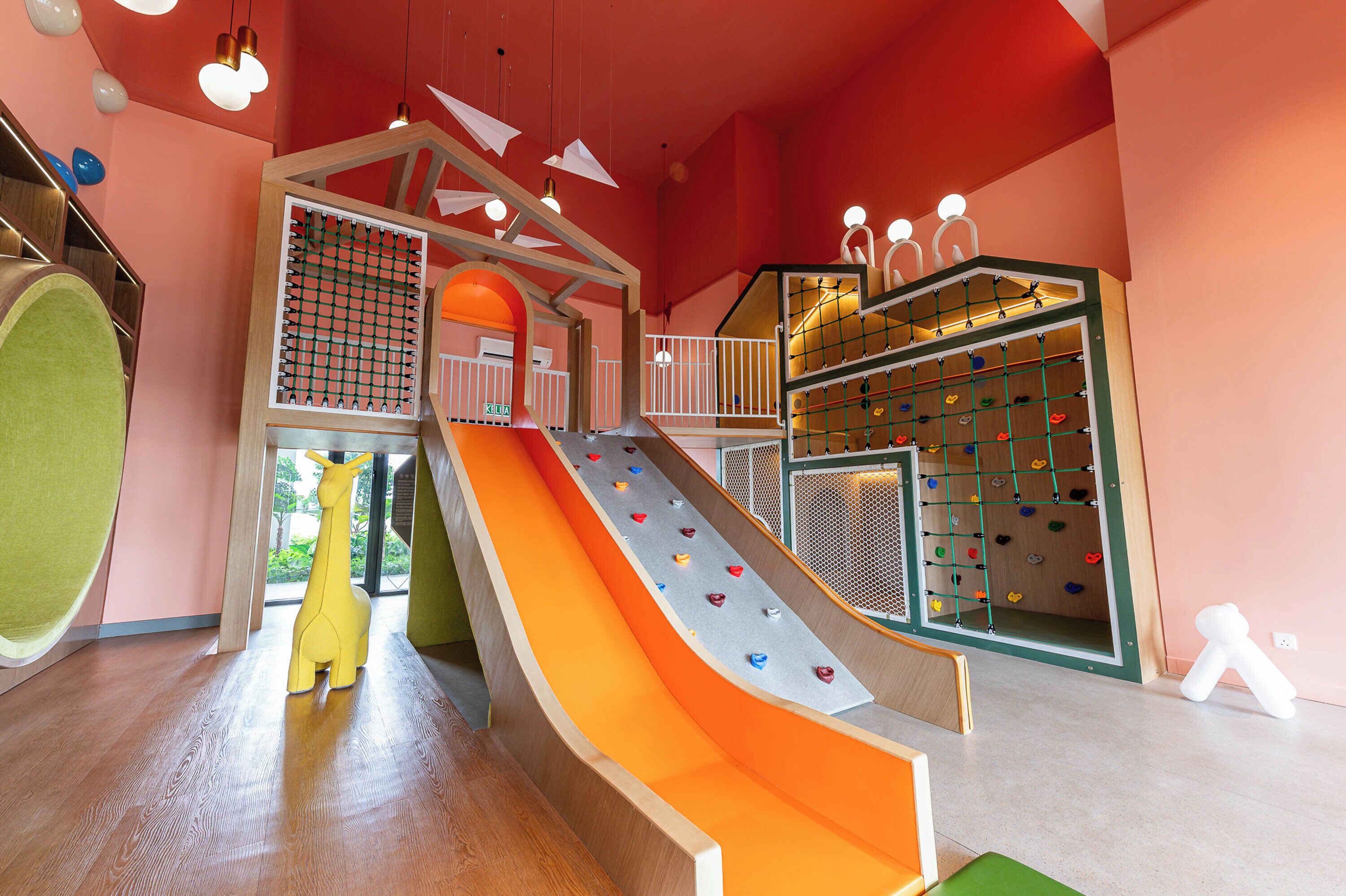 Un espace de jeux pour enfants avec un toboggan, un mur d’escalade et une décoration représentant une girafe.