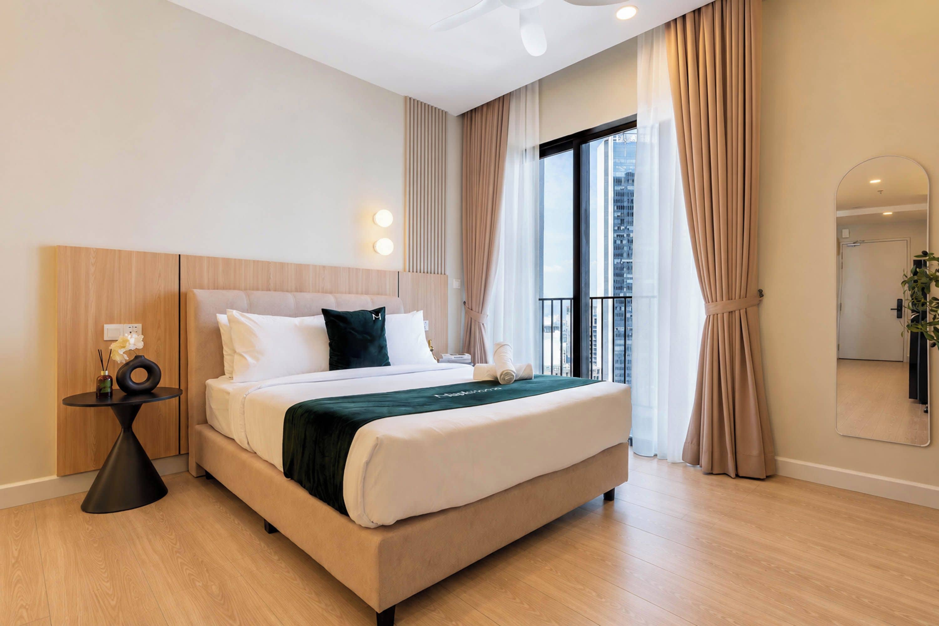 Une chambre d’hôtel moderne avec un grand lit, une table de chevet, un miroir et une vue sur la ville par la fenêtre.