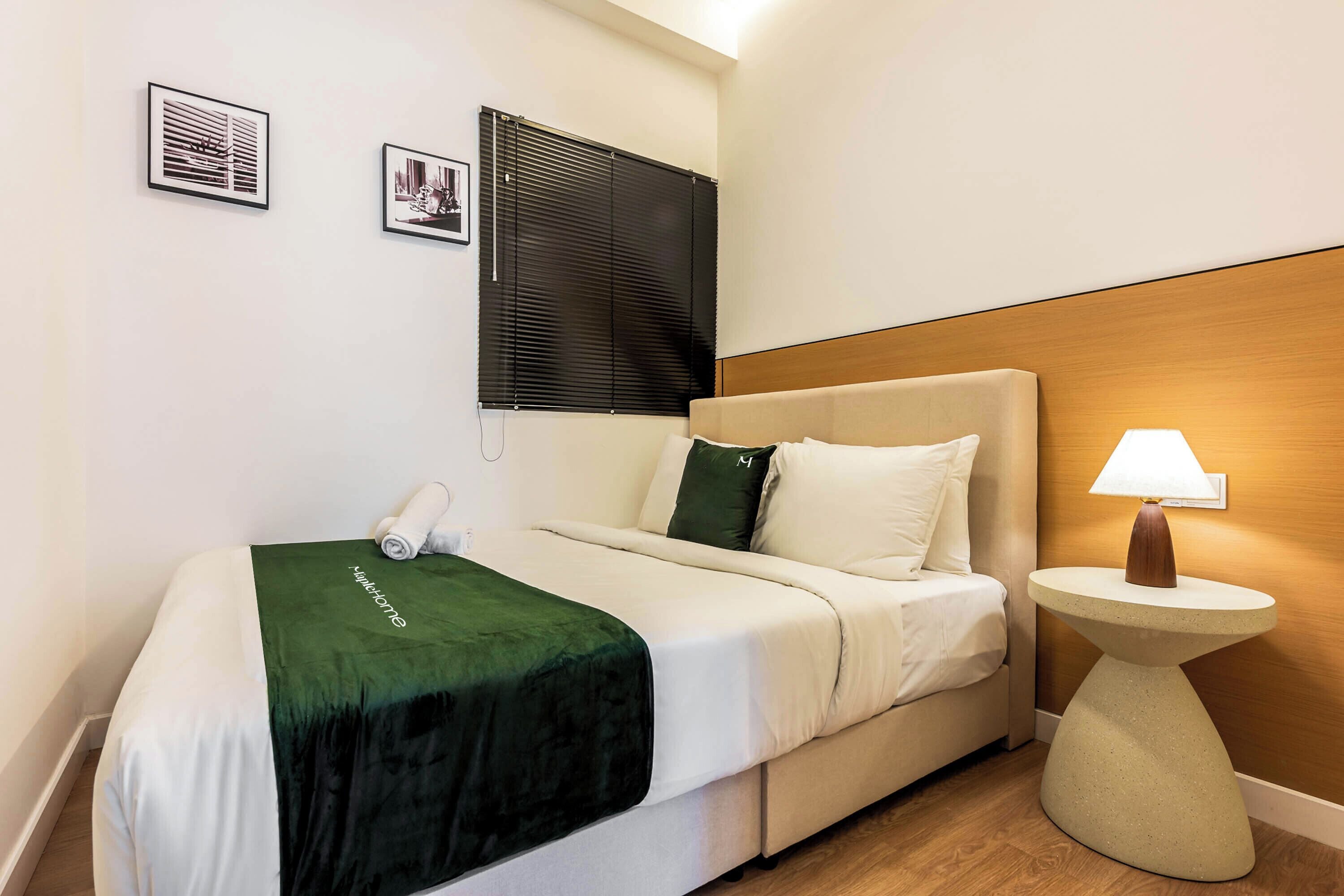 A hotel room with a bed, a bedside lamp, a headboard, a wall-mounted TV, and two framed pictures.