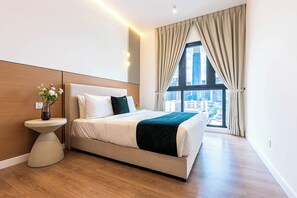 Un hotel moderno con una cama grande, una mesita de noche con un florero y vistas a la ciudad desde la ventana.