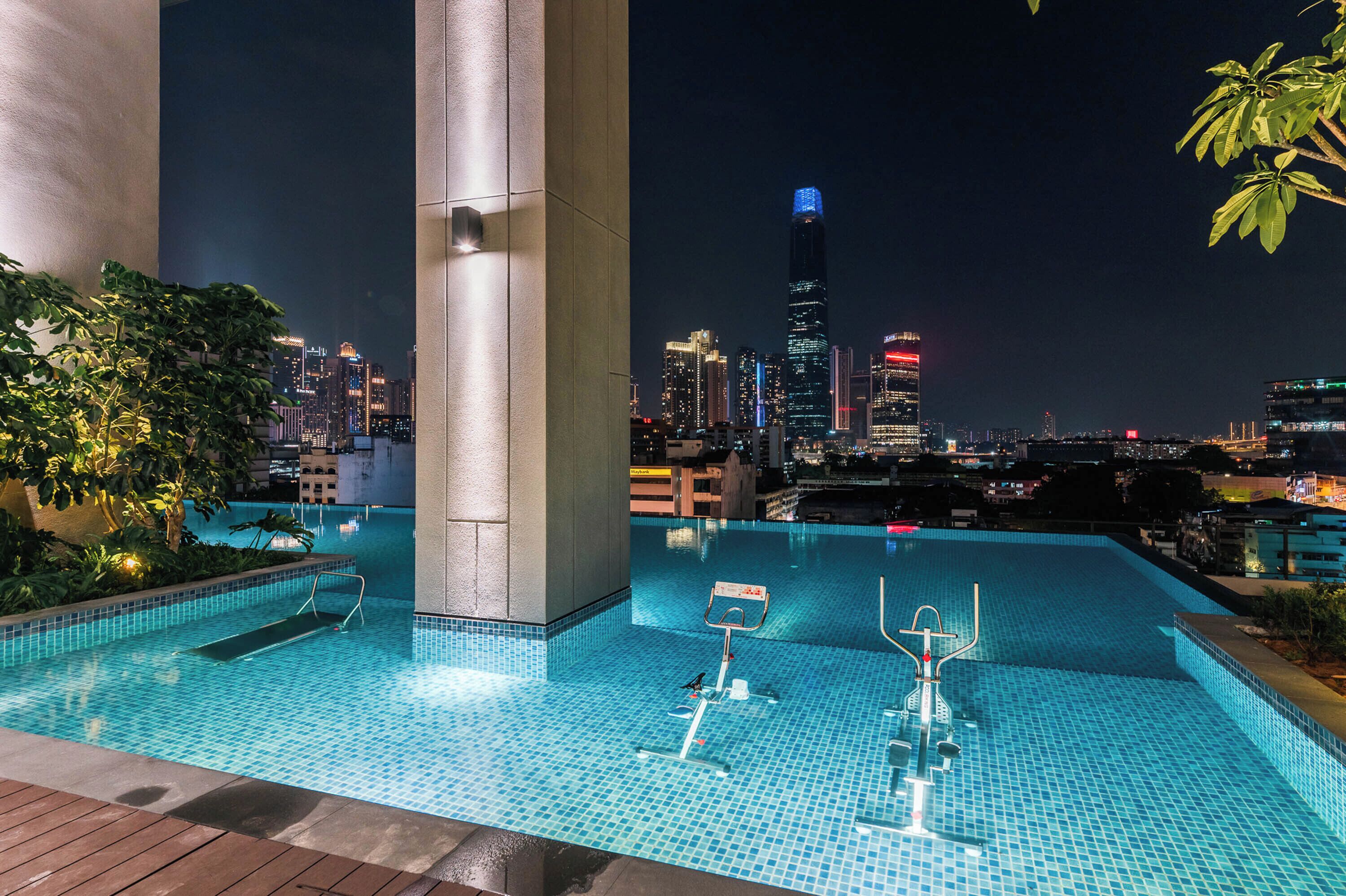An outdoor swimming pool with a cityscape view at night, including a prominent skyscraper.