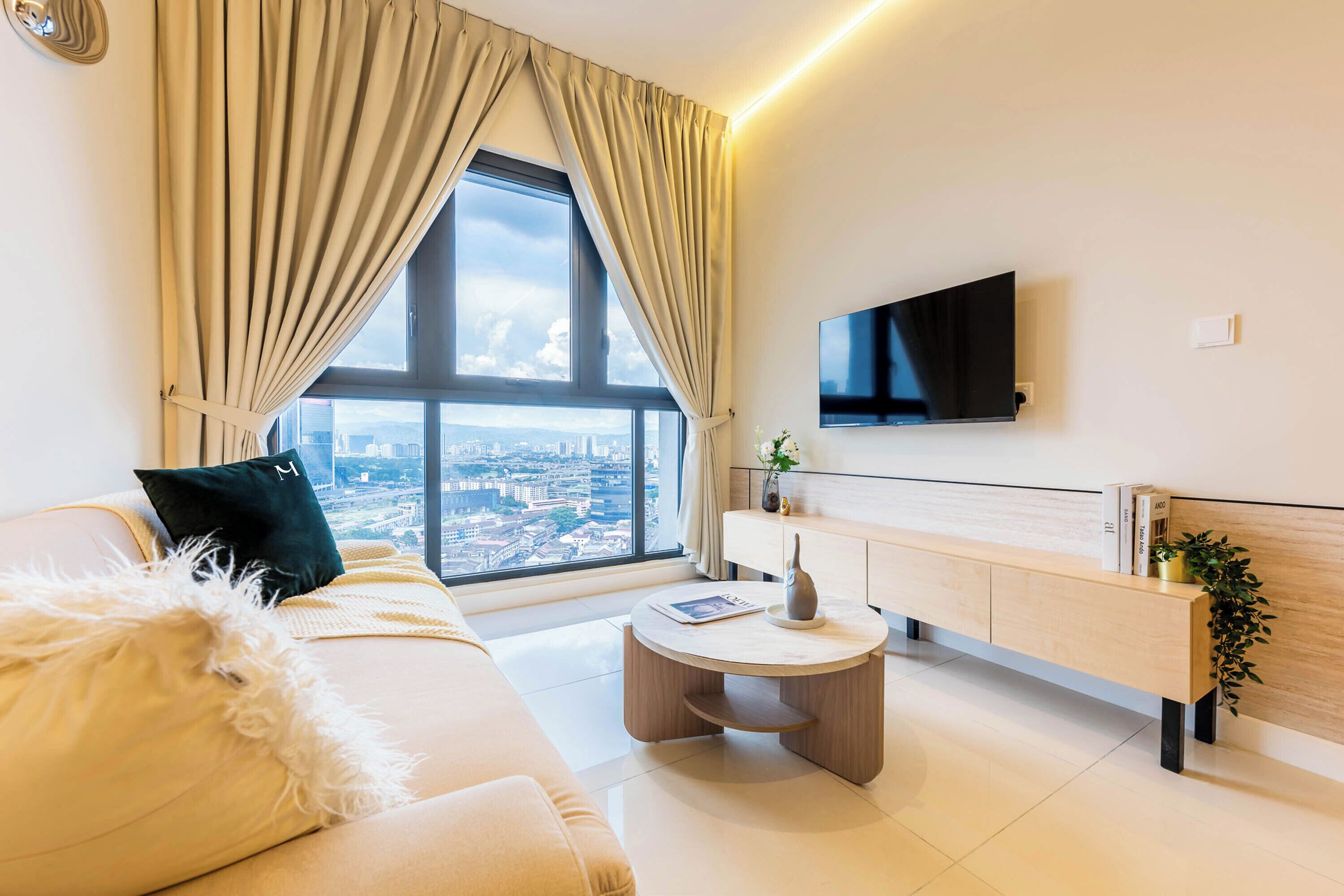 Un salon moderne avec un canapé, une table basse, un téléviseur fixé au mur et une vue sur la ville grâce à de grandes fenêtres.