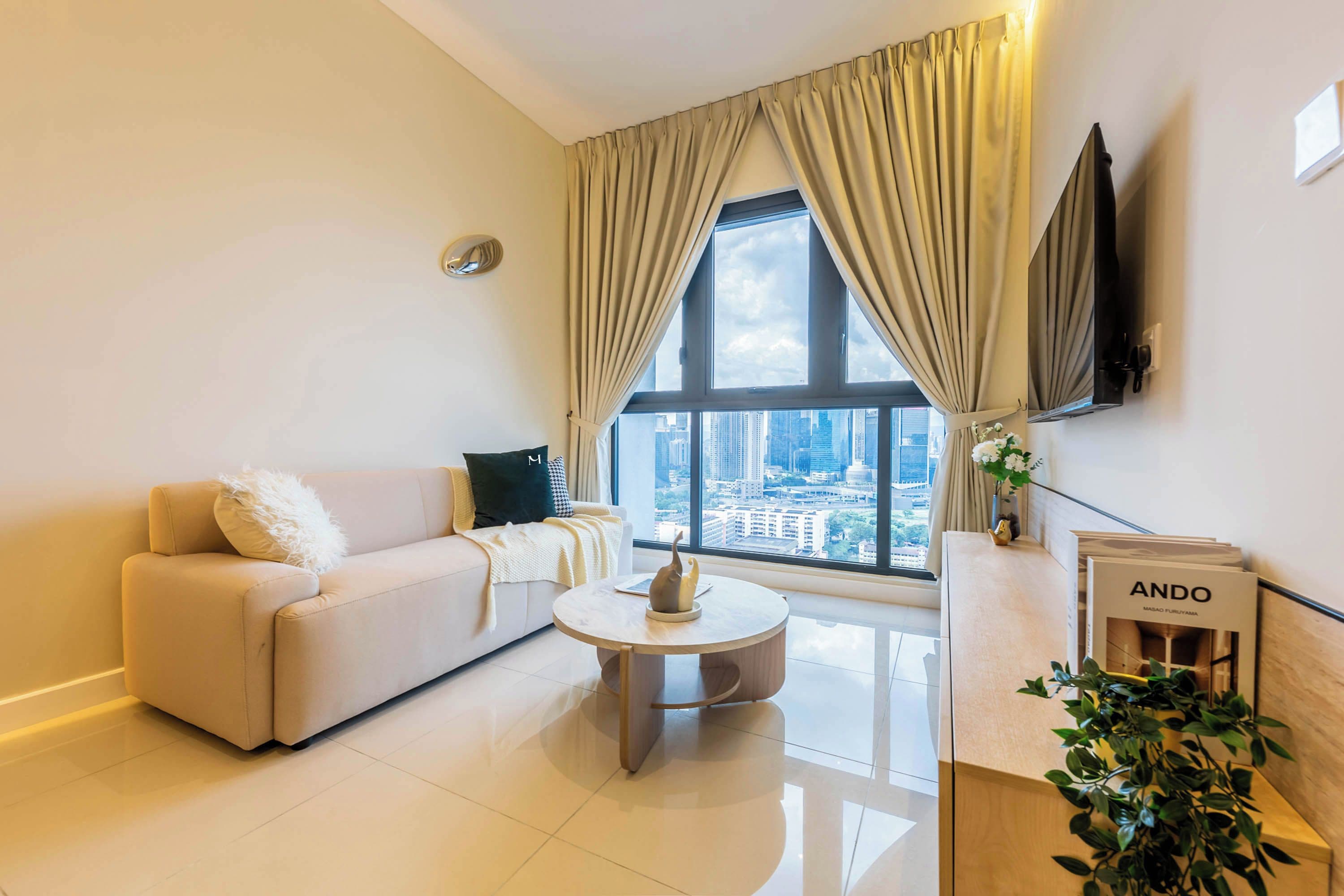 A modern living room with a sofa, a coffee table, and a view of a cityscape through large windows.