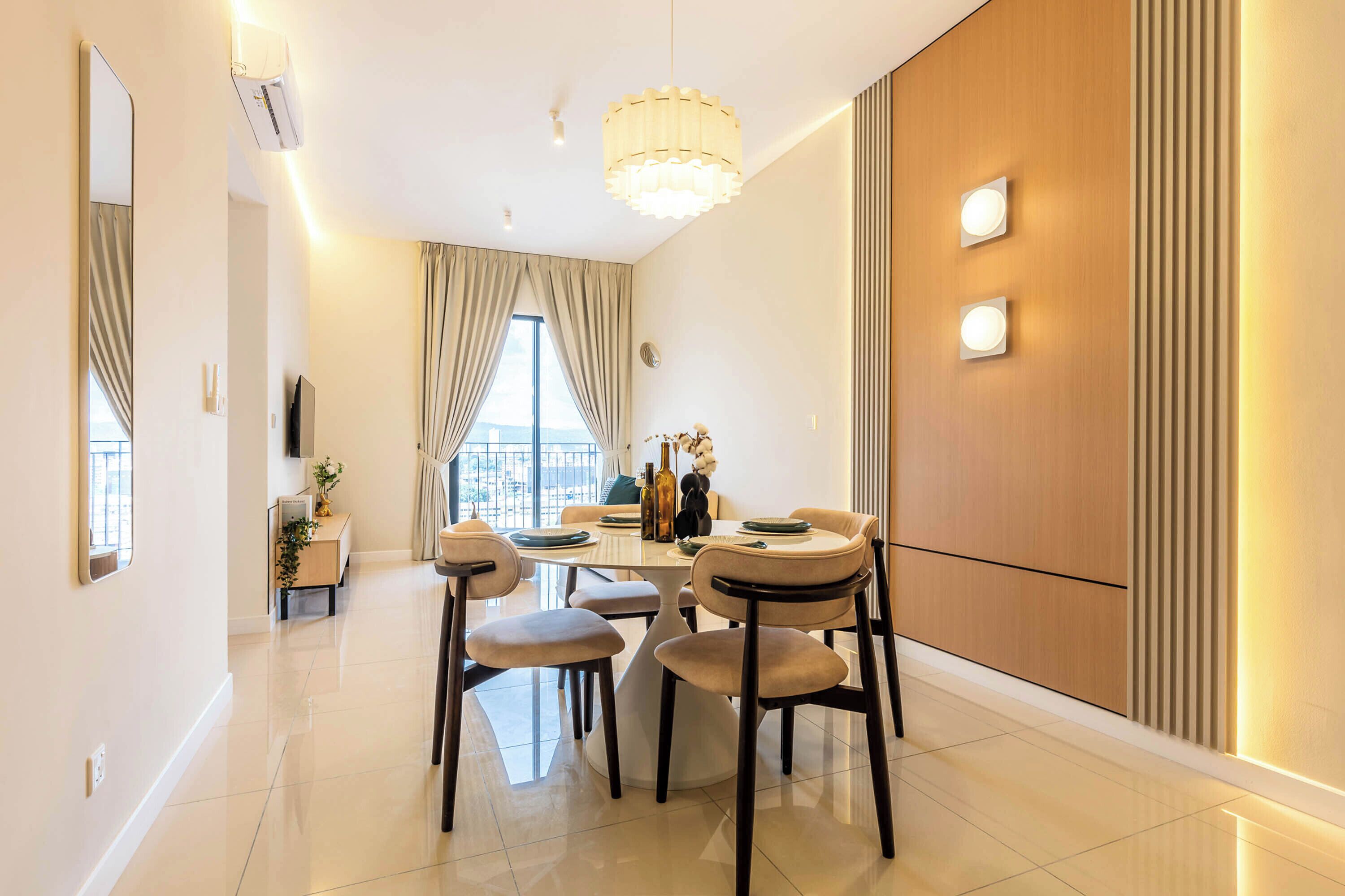 A modern dining area with a round table, four chairs, a chandelier, and a view through the window.