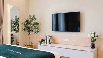 A modern bedroom with a bed, a TV mounted on the wall, a bedside table with books and a sign, and a small plant.