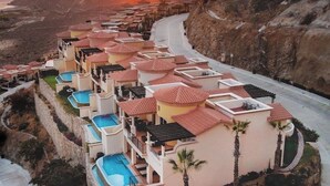 Ett semesterkomplex med flera byggnader, flera pooler och utsikt över solnedgången över ett bergigt landskap.