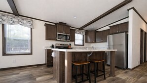 A modern kitchen with dark wood cabinets, a stainless steel refrigerator, and a central island with stools. - Northwoods Lakefront Retreat! Swim, Fish, Relax (Rhinelander)