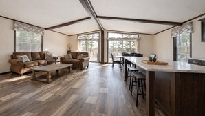 A spacious living room with a large sofa, a coffee table, and a kitchen area with a bar and stools. - Northwoods Lakefront Retreat! Swim, Fish, Relax (Rhinelander)