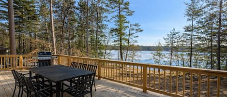 A deck with a table and chairs, overlooking a body of water and surrounded by trees.