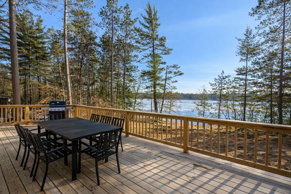 A deck with a table and chairs, overlooking a body of water and surrounded by trees. - Northwoods Lakefront Retreat! Swim, Fish, Relax (Rhinelander)