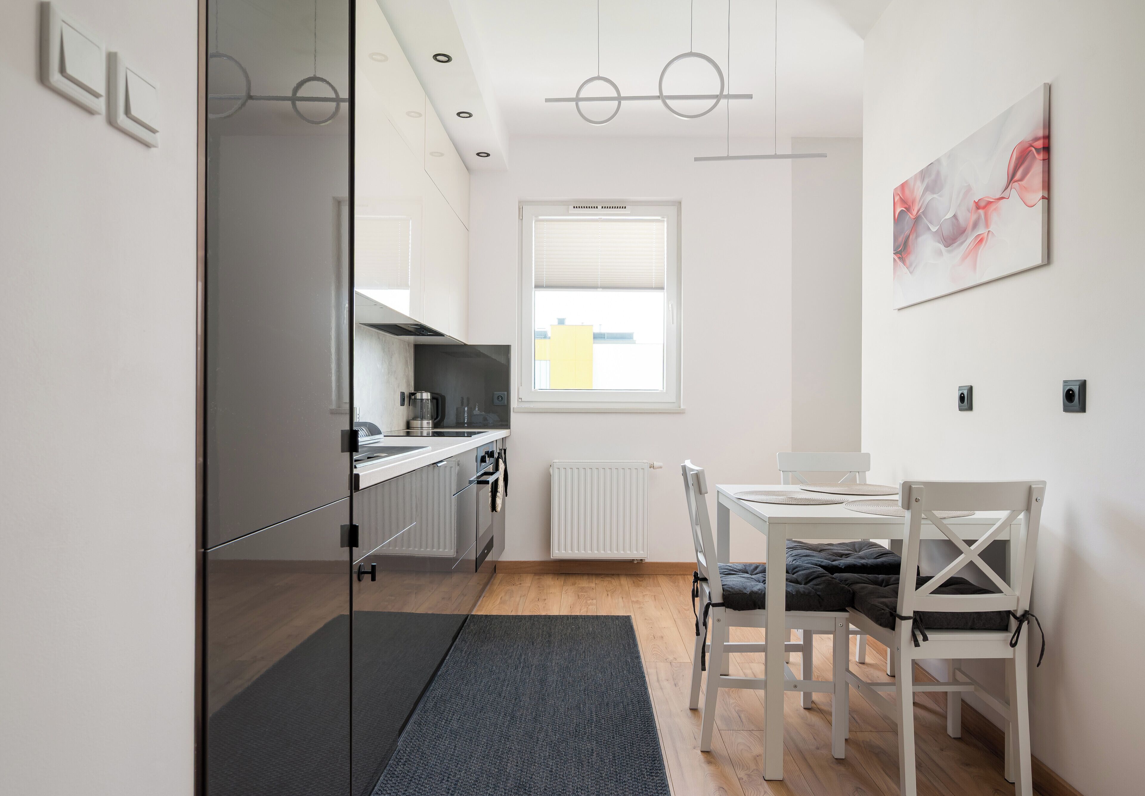 A modern kitchen with a dining area, a window with blinds, and a painting on the wall.