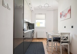 A modern kitchen with a dining area, a window with blinds, and a painting on the wall. - Modlińska Riverside Comfort Apartment (Warszawa)