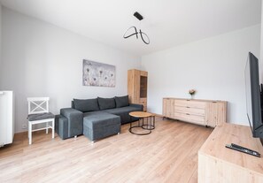 Un salon moderne avec un canapé gris, une table basse ronde en bois, une chaise blanche, un meuble en bois et un téléviseur.