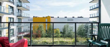 Un balcon avec un canapé rouge, un banc vert et une vue sur les bâtiments et la verdure environnants.