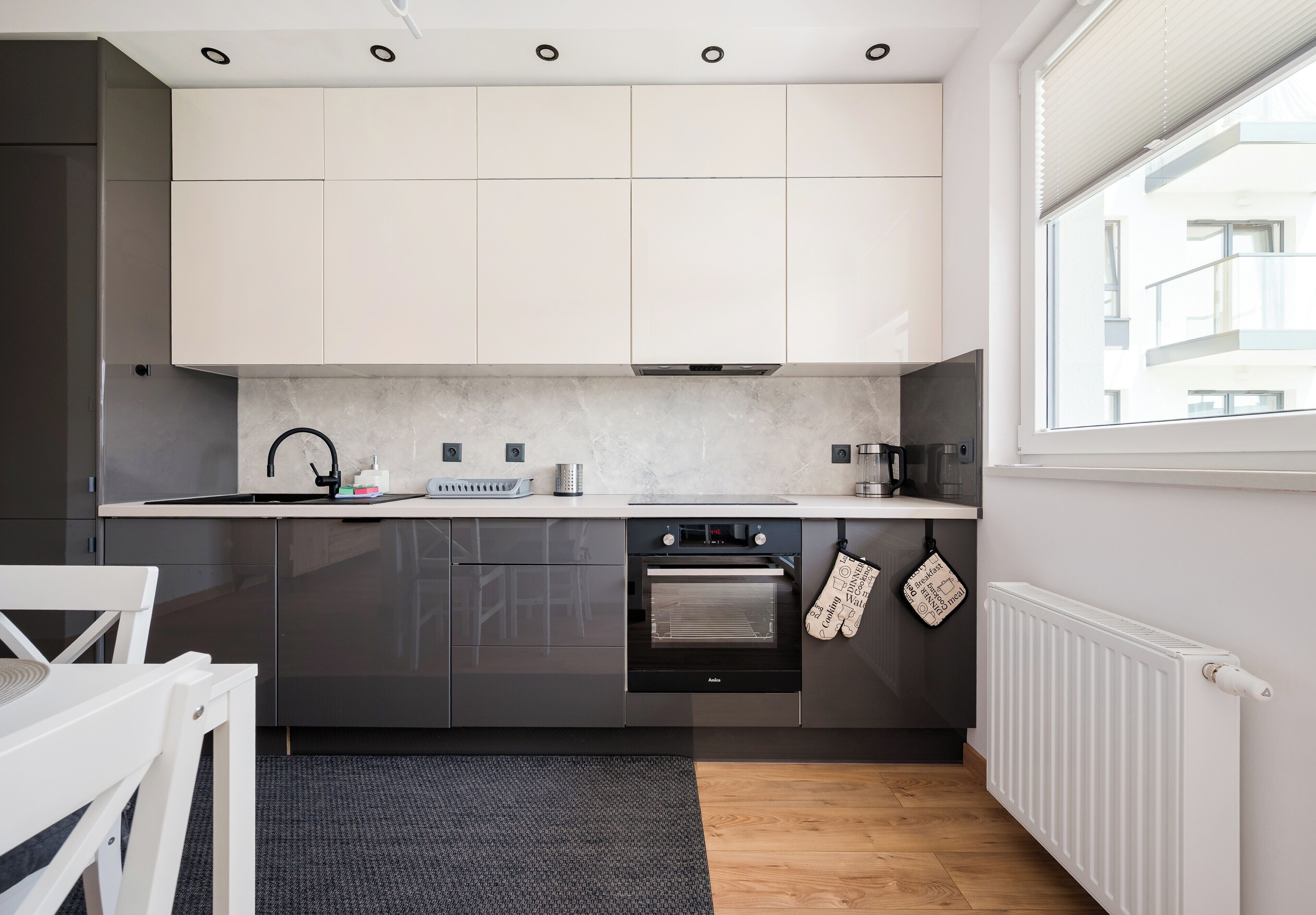 Une cuisine moderne dotée d’un four encastré, d’une fenêtre avec stores et offrant une vue sur l’extérieur.
