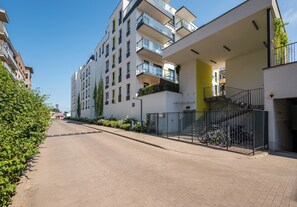 Ein modernes Mehrfamilienhaus mit mehreren Balkonen, einem verschlossenen Eingangsbereich und blauem Himmel.