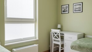 A room with a window, radiator, desk, chair, bed, and two framed pictures on the wall. - Modlińska Riverside Comfort Apartment (Warszawa)