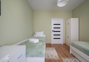 A small, single-bed room with a green bedspread, a white wardrobe, and a door with horizontal black stripes. - Modlińska Riverside Comfort Apartment (Warszawa)