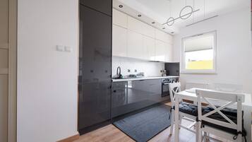 A modern kitchen with a built-in oven, a dining area with a white table and chairs, and a window with blinds.